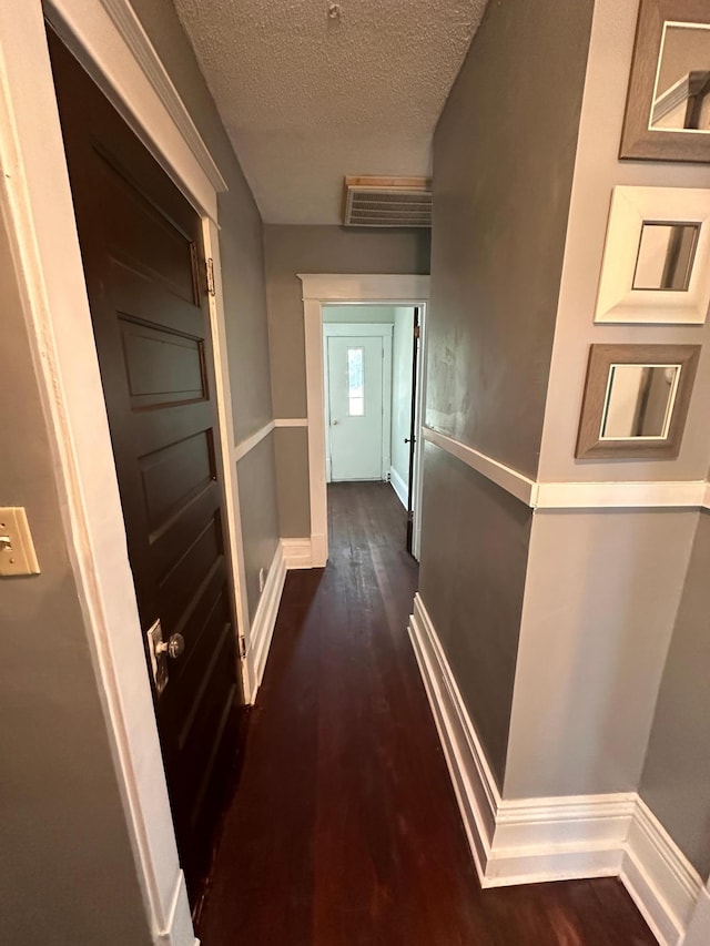 corridor with dark wood-style floors, visible vents, a textured ceiling, and baseboards