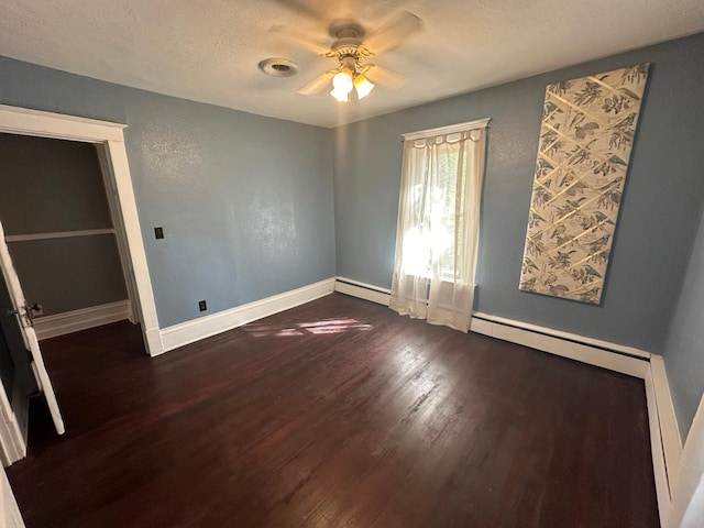 unfurnished bedroom featuring dark wood-type flooring, a baseboard heating unit, a ceiling fan, a textured ceiling, and baseboards