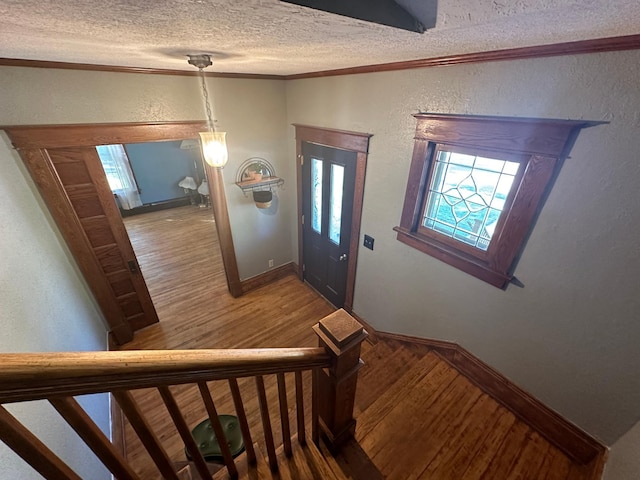 foyer with ornamental molding, a textured wall, a textured ceiling, and wood finished floors