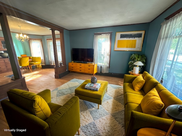 living room featuring crown molding, a notable chandelier, decorative columns, light wood-style flooring, and baseboards