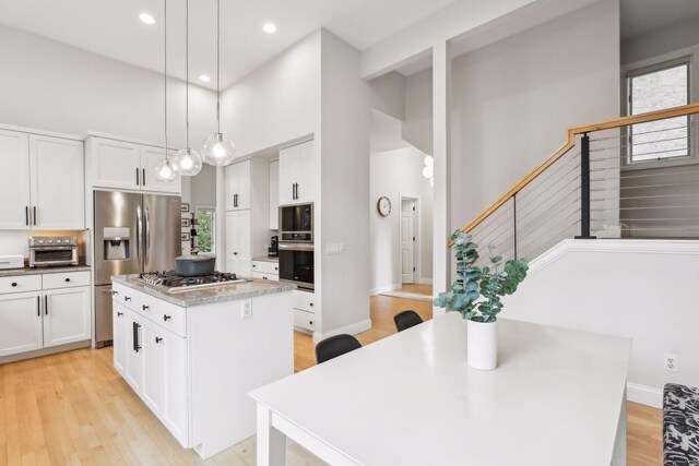 kitchen featuring pendant lighting, light hardwood / wood-style floors, a center island, stainless steel appliances, and a towering ceiling