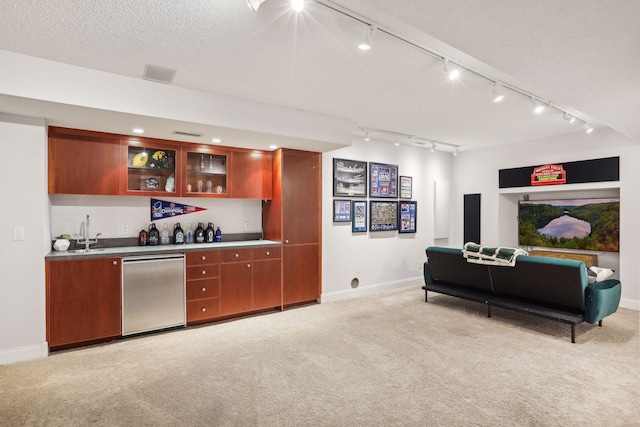 kitchen featuring a textured ceiling, dishwasher, sink, light colored carpet, and track lighting