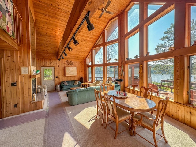 carpeted dining space with wood walls, high vaulted ceiling, a water view, and rail lighting