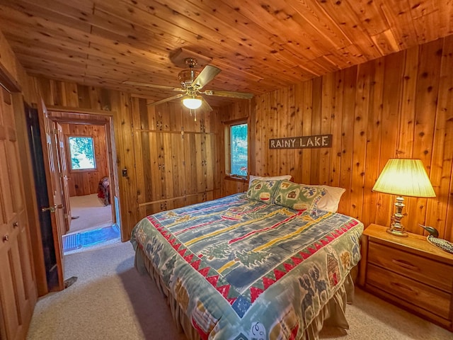 carpeted bedroom with wood walls, multiple windows, wooden ceiling, and ceiling fan