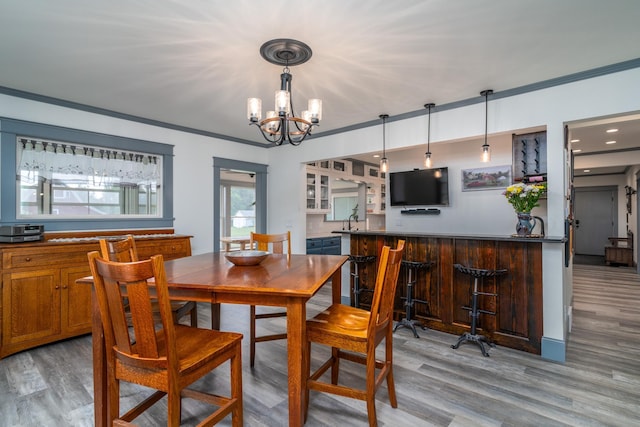 dining room with ornamental molding, light hardwood / wood-style floors, wet bar, and an inviting chandelier