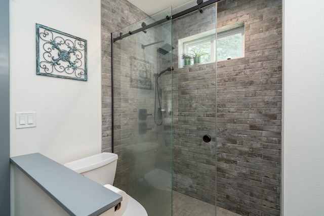 bathroom featuring a shower with door and toilet