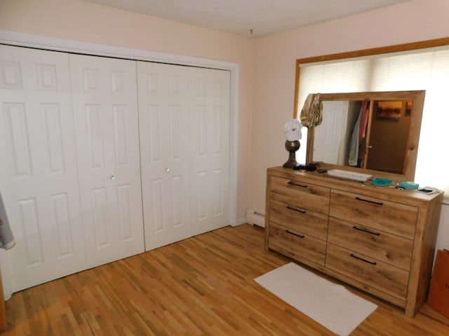 bedroom featuring baseboard heating, light hardwood / wood-style flooring, and a closet