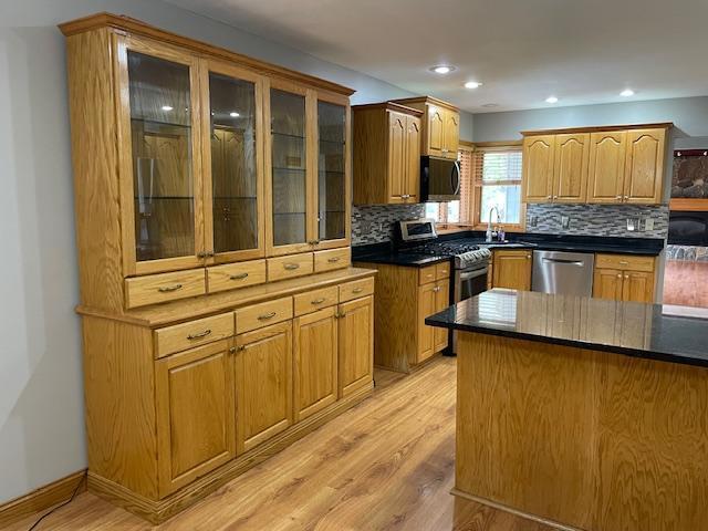 675 10th St, Granite Falls, MN 56241 - kitchen with stainless steel appliances, light wood-style flooring, backsplash, dark countertops, and glass insert cabinets