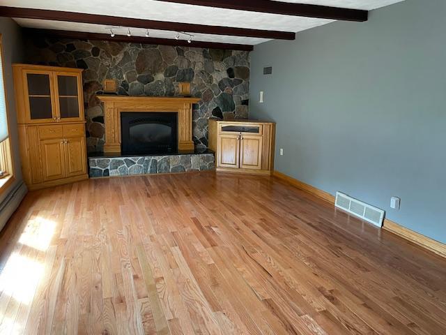 675 10th St, Granite Falls, MN 56241 - unfurnished living room featuring track lighting, light wood finished floors, beamed ceiling, and a stone fireplace