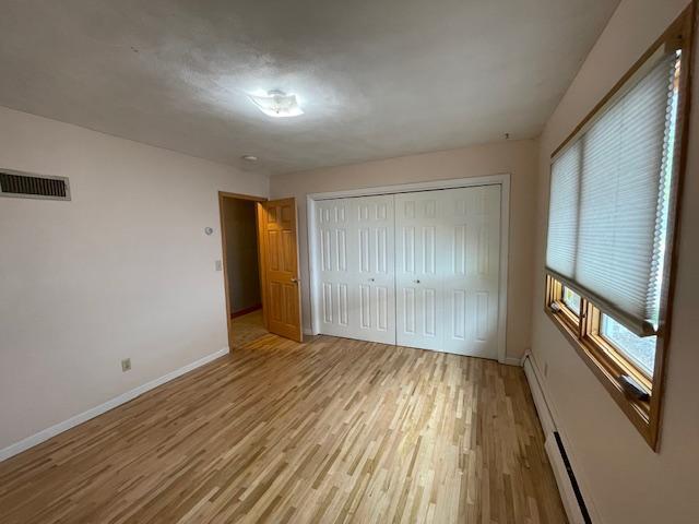 675 10th St, Granite Falls, MN 56241 - unfurnished bedroom featuring light wood-style floors, a baseboard radiator, and a closet
