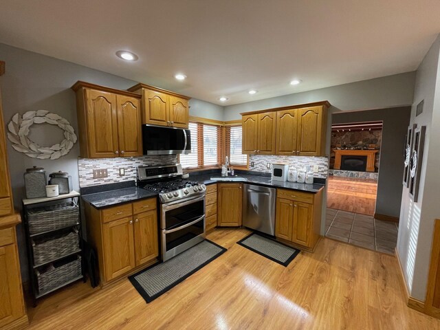 675 10th St, Granite Falls, MN 56241 - kitchen with appliances with stainless steel finishes, decorative backsplash, brown cabinets, light wood-style flooring, and a glass covered fireplace