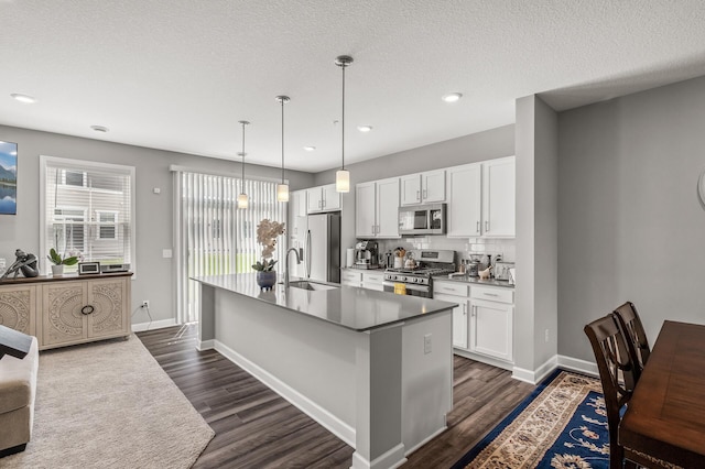 kitchen with white cabinetry, dark wood-type flooring, appliances with stainless steel finishes, and an island with sink