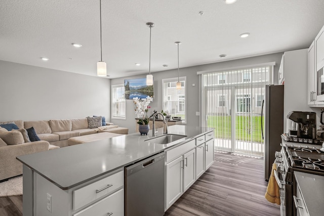 kitchen featuring appliances with stainless steel finishes, a center island with sink, sink, light wood-type flooring, and white cabinetry