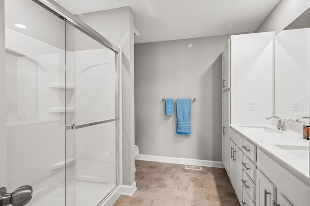 bathroom featuring parquet floors, a shower with shower door, toilet, and double sink vanity