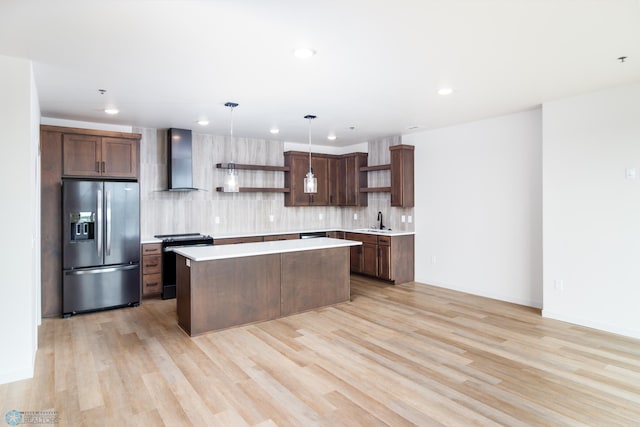 kitchen featuring stainless steel refrigerator with ice dispenser, wall chimney exhaust hood, black range oven, sink, and decorative light fixtures