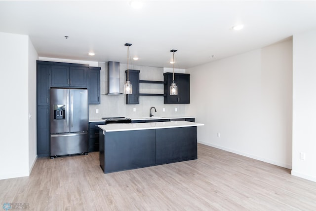 kitchen with hanging light fixtures, a center island, sink, wall chimney range hood, and stainless steel fridge with ice dispenser