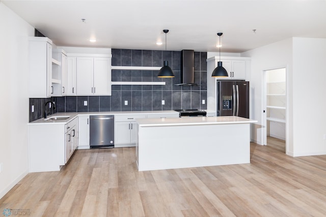 kitchen featuring decorative backsplash, appliances with stainless steel finishes, wall chimney exhaust hood, sink, and hanging light fixtures