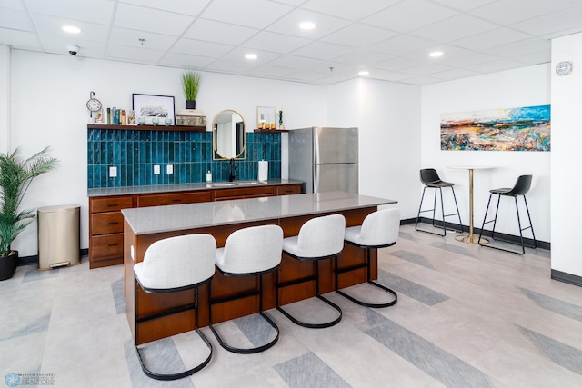 kitchen featuring a kitchen breakfast bar, a center island, stainless steel refrigerator, sink, and a paneled ceiling