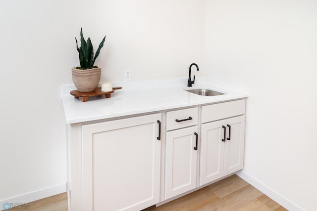 bar featuring a sink, baseboards, and light wood finished floors