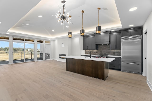 kitchen featuring a raised ceiling, built in refrigerator, light hardwood / wood-style flooring, and pendant lighting