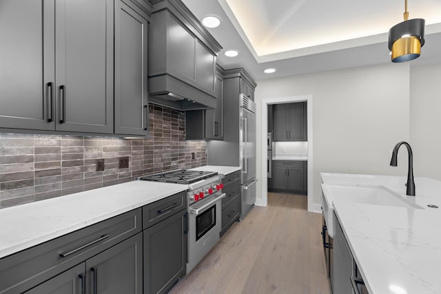 kitchen featuring gray cabinetry, high end appliances, sink, light hardwood / wood-style flooring, and light stone counters