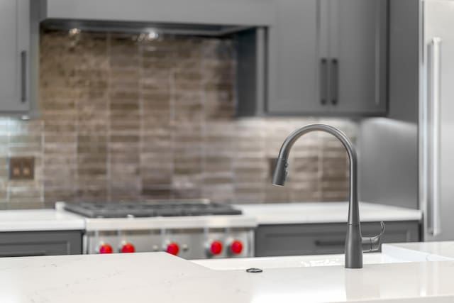 interior details with gray cabinetry, decorative backsplash, light stone counters, and range