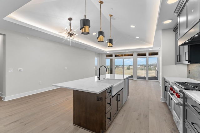 kitchen with sink, pendant lighting, a raised ceiling, and a kitchen island with sink