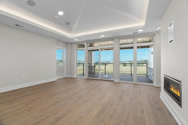 unfurnished living room with light wood-type flooring and a raised ceiling