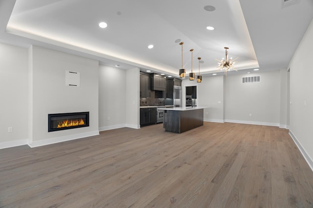 kitchen with wood-type flooring, decorative light fixtures, a raised ceiling, and a kitchen island