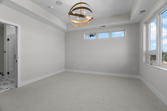 spare room featuring a tray ceiling, carpet, and a chandelier