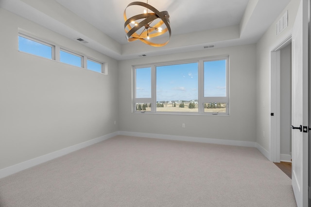 spare room with light colored carpet, a raised ceiling, and a notable chandelier