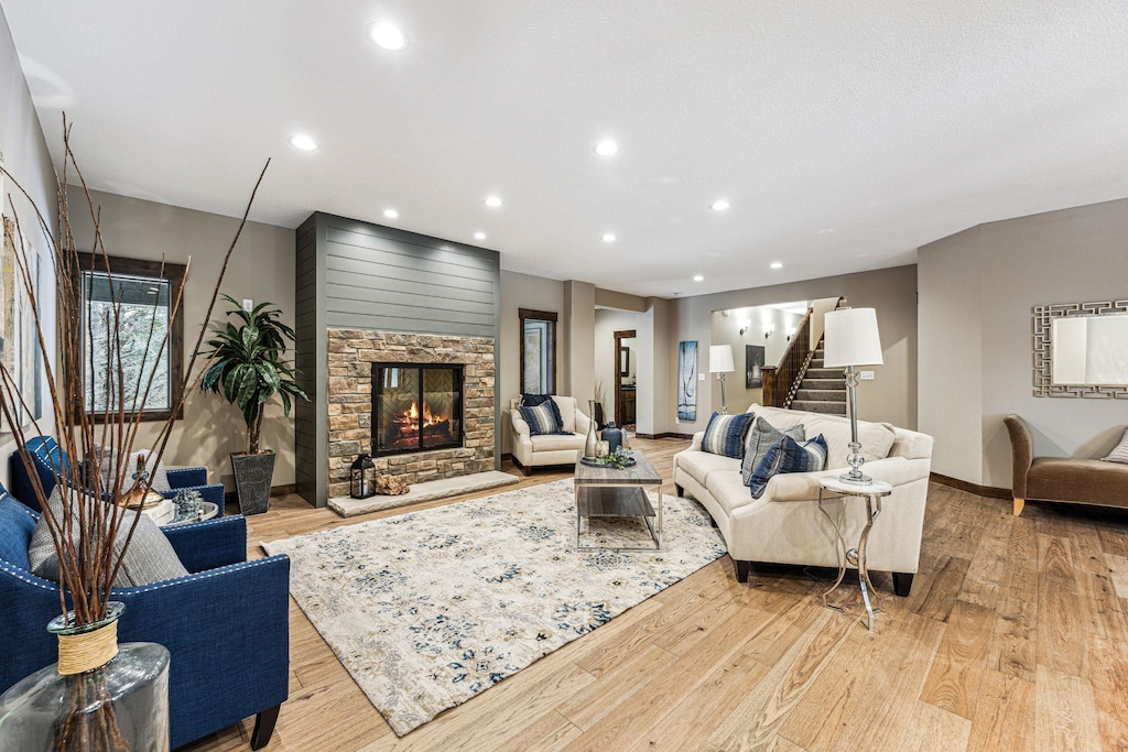 living area with light wood-type flooring, recessed lighting, stairway, and a stone fireplace