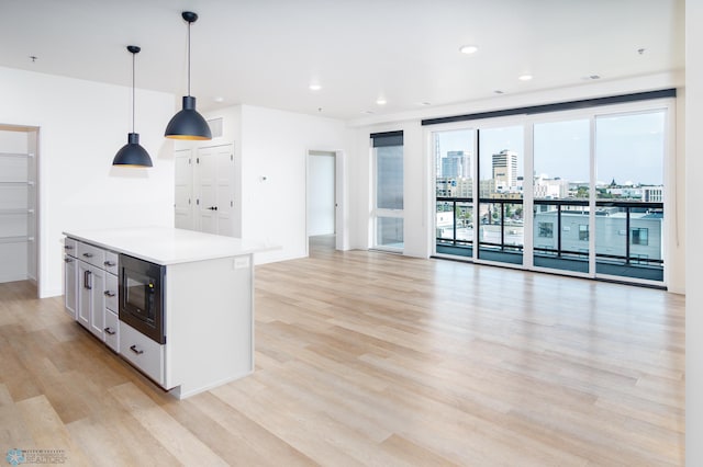 kitchen with pendant lighting, a kitchen island, black microwave, and light hardwood / wood-style flooring