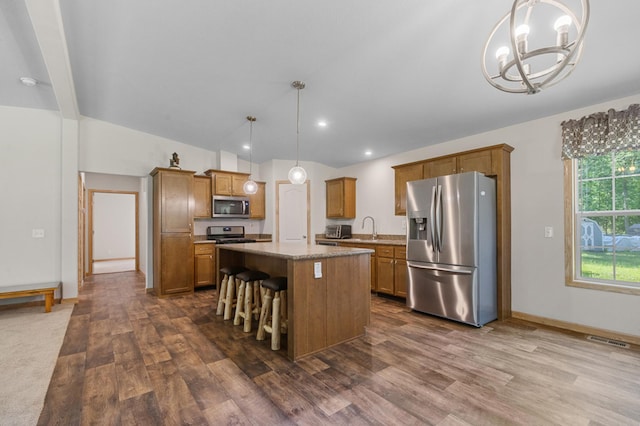 kitchen featuring stainless steel appliances, a chandelier, a center island, dark wood-style flooring, and brown cabinets