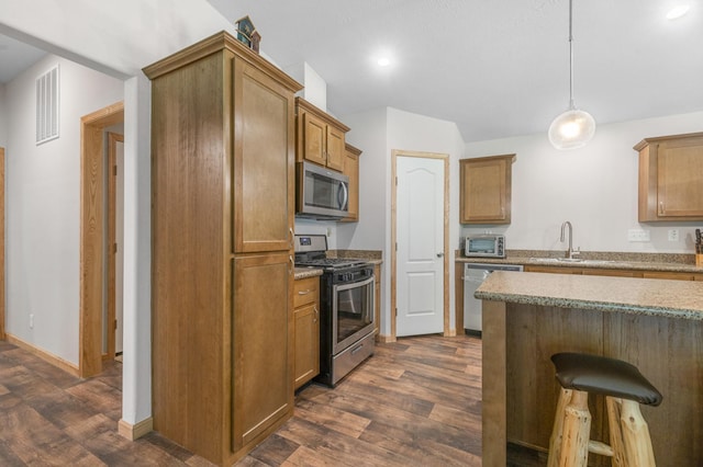 kitchen featuring appliances with stainless steel finishes, hanging light fixtures, a breakfast bar, sink, and dark wood-type flooring