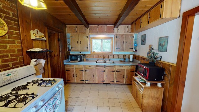 kitchen with beam ceiling, stainless steel microwave, wooden walls, light tile patterned floors, and white range oven