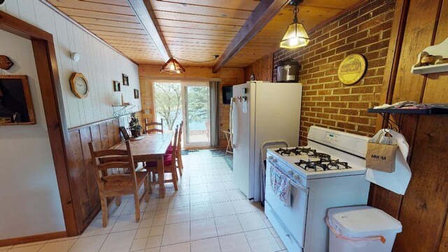 kitchen with white appliances, light tile patterned floors, beamed ceiling, brick wall, and pendant lighting