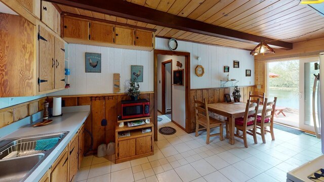 kitchen featuring beam ceiling, stainless steel microwave, and light tile patterned floors