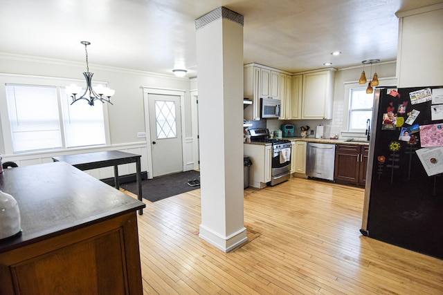 kitchen featuring stainless steel appliances, crown molding, decorative light fixtures, cream cabinetry, and light hardwood / wood-style floors