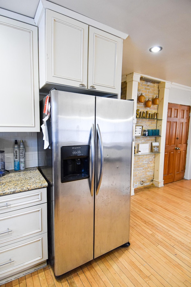 kitchen featuring light stone countertops, stainless steel fridge, light hardwood / wood-style floors, decorative backsplash, and white cabinets