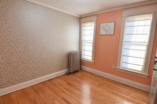 empty room featuring radiator heating unit, light wood-type flooring, ornamental molding, and a healthy amount of sunlight