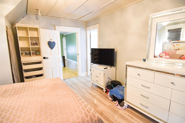 bedroom featuring light wood-type flooring, a textured ceiling, and wooden walls