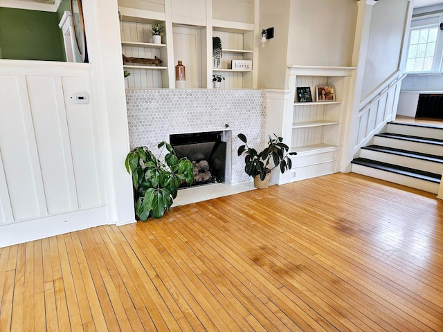 living room with a tile fireplace, built in shelves, and light hardwood / wood-style floors