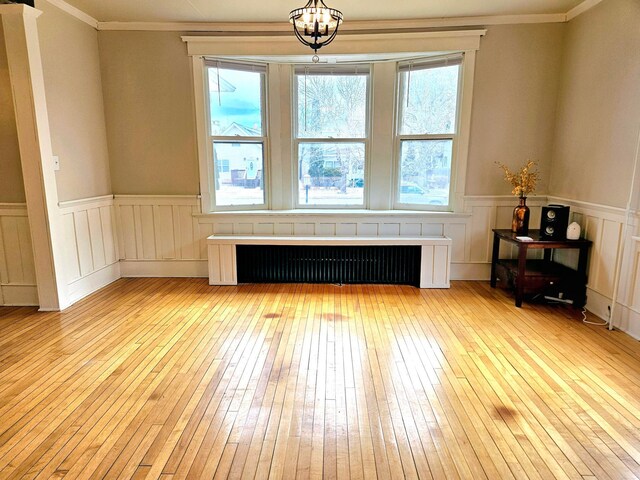 721 Labree Ave N, Thief River Falls, MN 56701 - unfurnished living room with radiator, light wood-style floors, a wainscoted wall, crown molding, and a chandelier