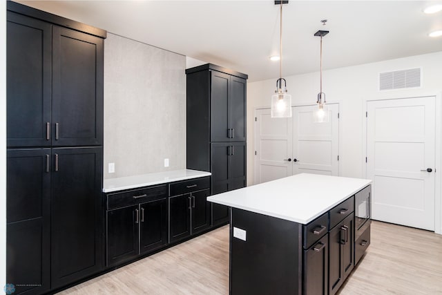 kitchen with light hardwood / wood-style floors, a kitchen island, hanging light fixtures, and built in microwave