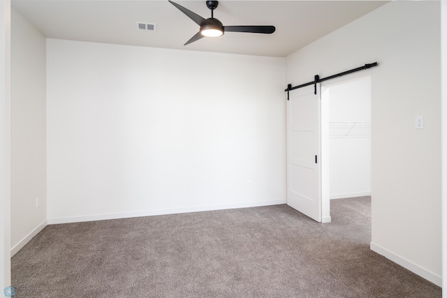 carpeted empty room featuring a barn door and ceiling fan