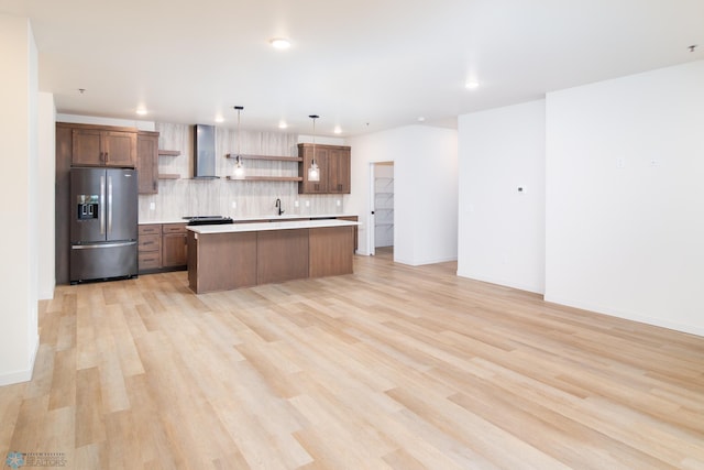 kitchen with a center island, hanging light fixtures, tasteful backsplash, stainless steel fridge, and light hardwood / wood-style floors