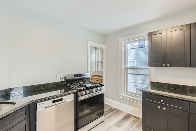 kitchen with range with gas stovetop, dark stone counters, dark brown cabinets, light hardwood / wood-style floors, and stainless steel dishwasher