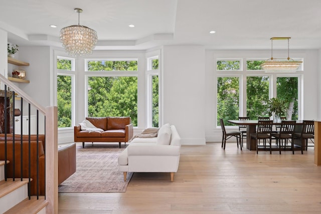 living room with a notable chandelier, light hardwood / wood-style flooring, a wealth of natural light, and a tray ceiling