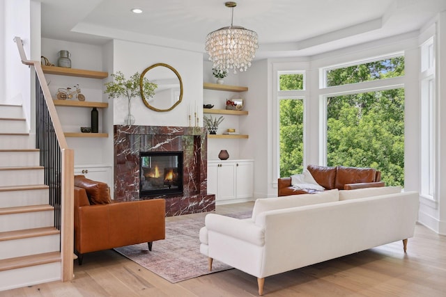 living room featuring a high end fireplace, a tray ceiling, light hardwood / wood-style flooring, and a notable chandelier